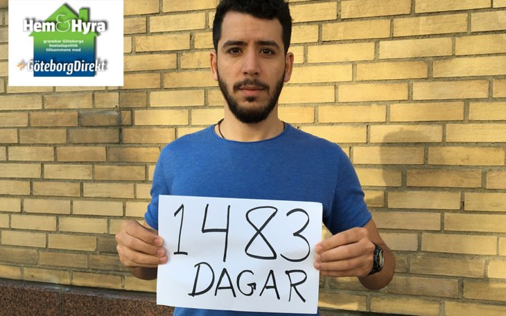 Jihad Eshmawi håller upp en textad skylt där det står "1 483 dagar" framför en husfasad.