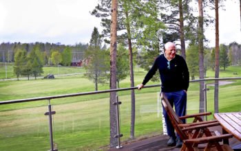 Kjell Guldbrand står lutad mot ett räcke. I bakgrunden syns golfbanan.