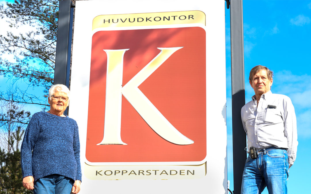 En kvinna och en man som står på varsin sida om en stor skylt med Kopparstadens logga på.