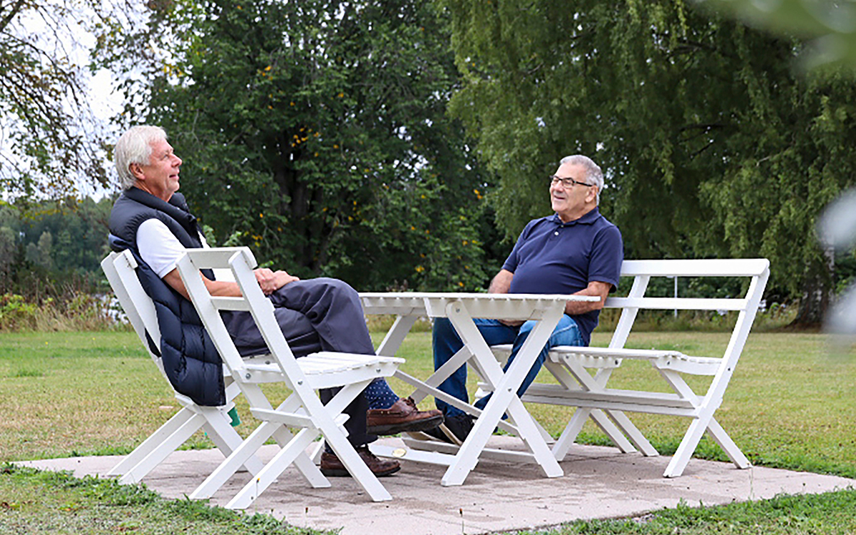 Två män sitter vid en trädgårdsmöbel och samtalar.