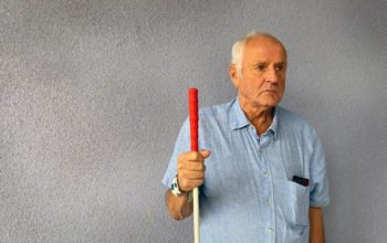 Äldre man mot vägg med blindkäpp