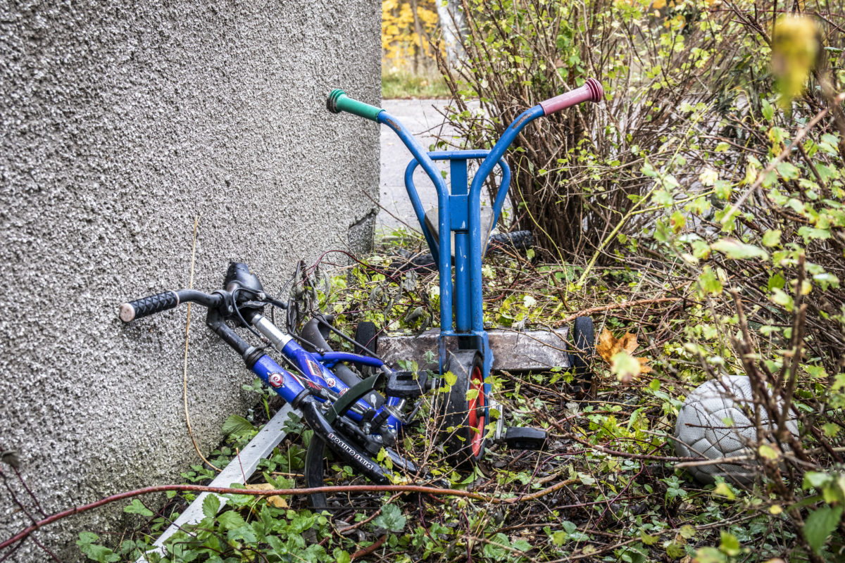 Ett par övergivna barncyklar står lutade mot en av husväggarna.