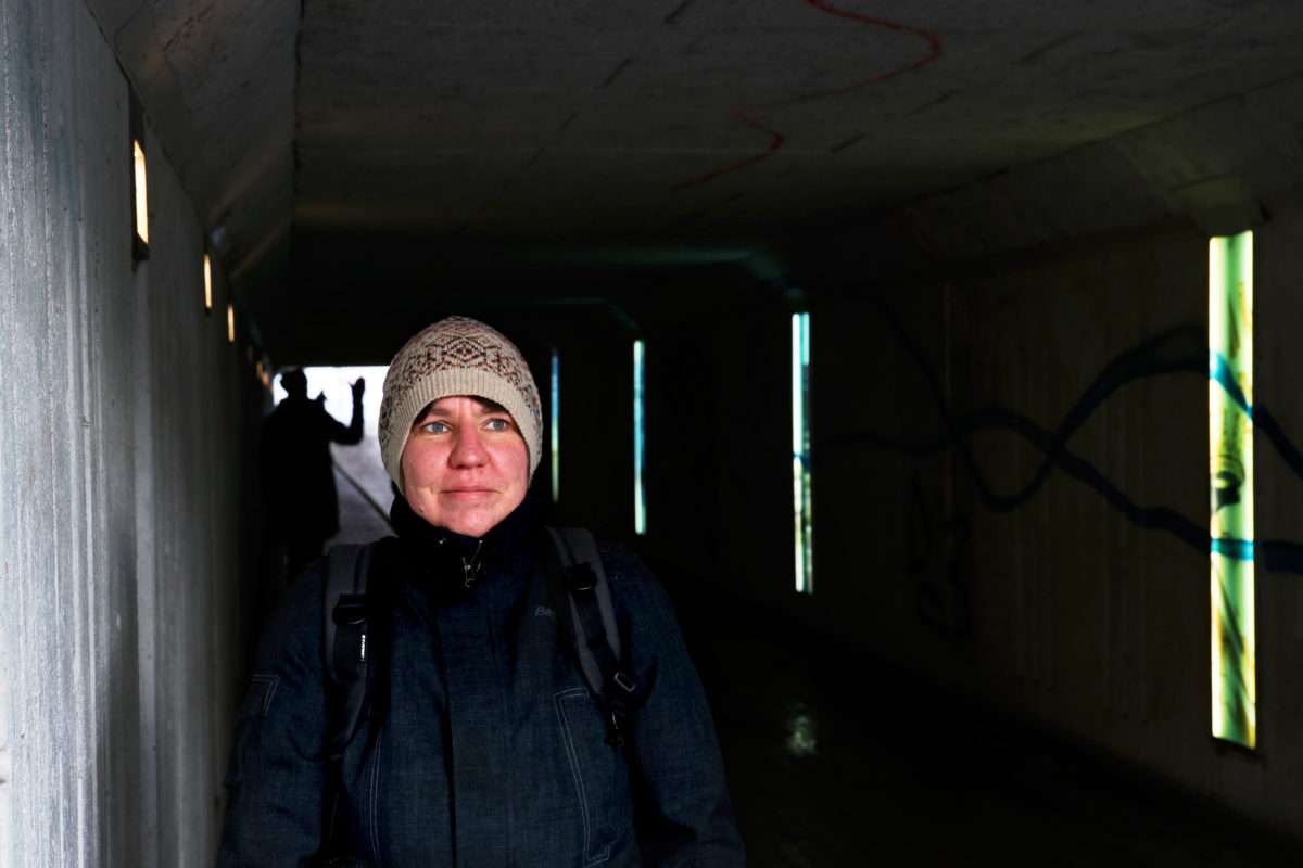 Kvinna med mössa står i tunnel med ljus och siluett i bakgrunden.