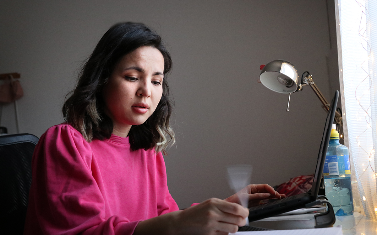 Kvinna i svart hår och rosa tröja sitter vid ett skrivbord