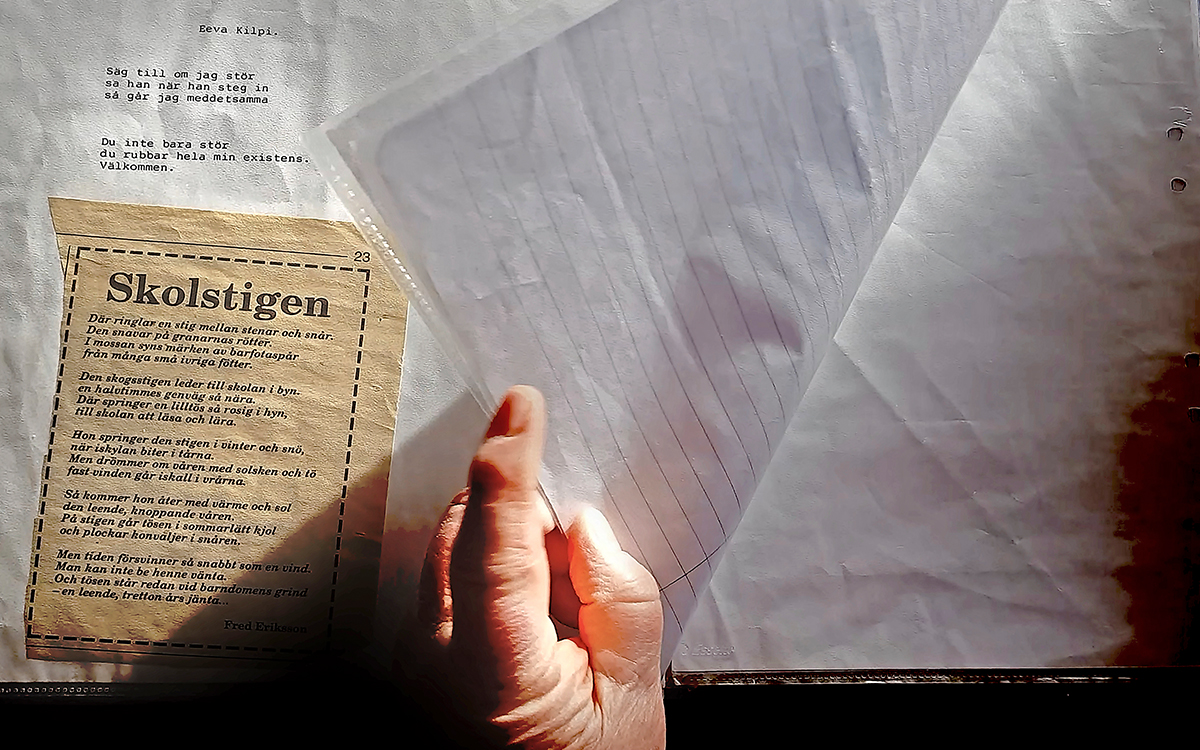 En hand som bläddrar med paper. Vid sidan ligger ett gulnat tidningsklipp med en dikt.