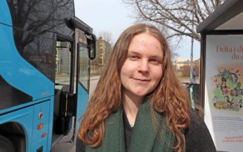 Livia Jönsson står bredvid en buss. Hon har långt hår.