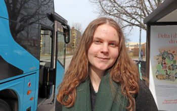 Livia Jönsson står bredvid en buss. Hon har långt hår.