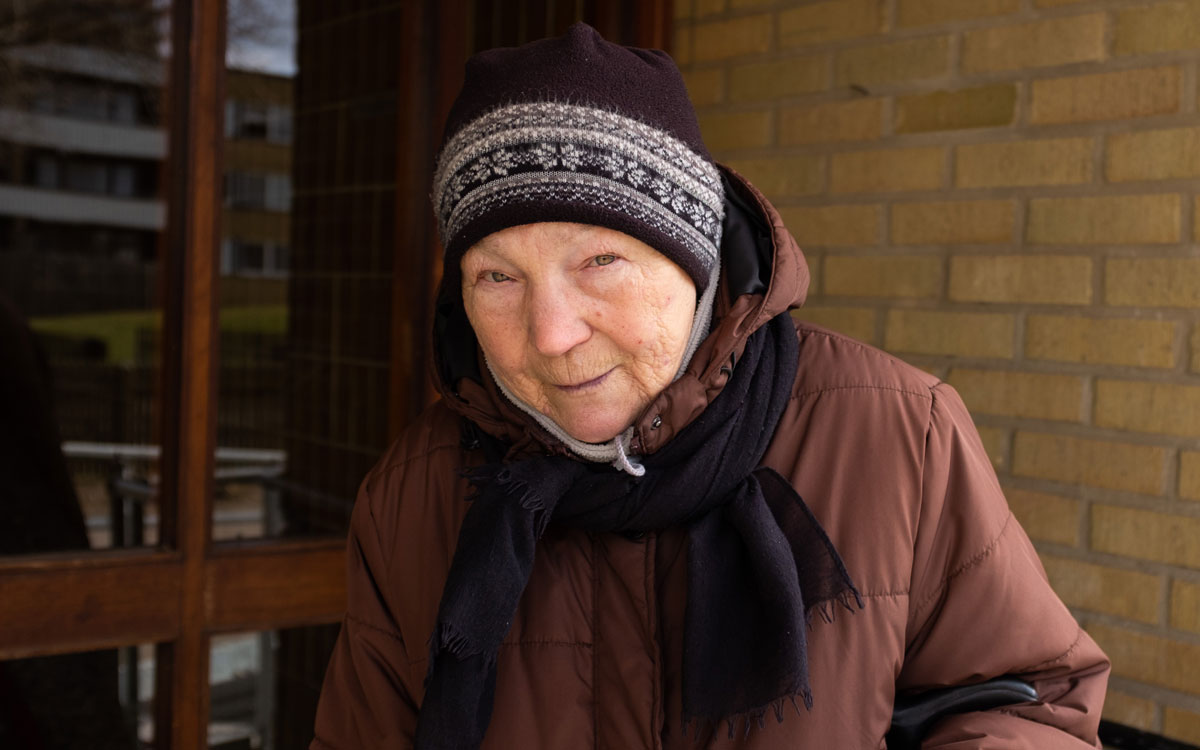 En äldre kvinna i brun kappa och med mössa med mönster på.
