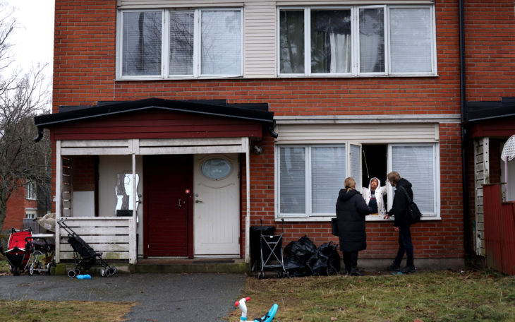 Ett radhus i rött tegel där två personer talar med en kvinna genom ett öppet fönster.