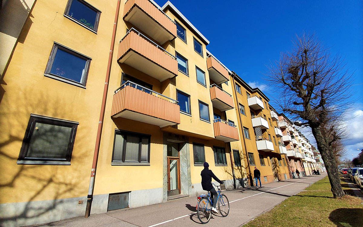 Ett hyreshus med gul fasad. Framför huset passerar en person på cykel.