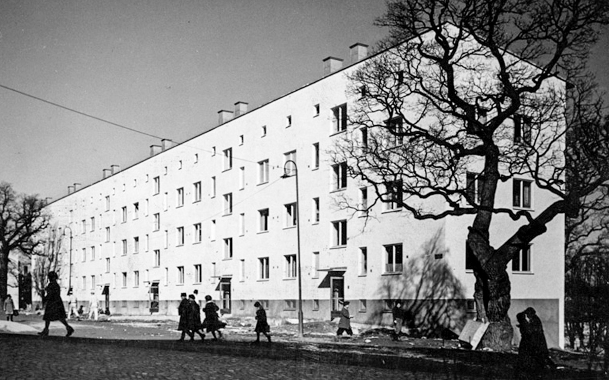 Gammalt svartvitt foto på ett barnrikehus i Kristineberg, Stockholm. I förgrunden syns barn som mörka silhuetter.