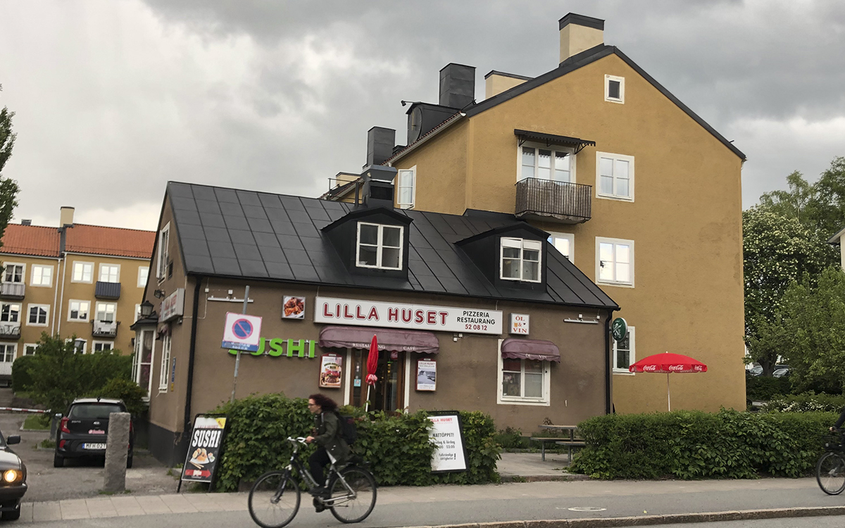 Gamla Studentstaden, en person cyklar förbi pizzerian Lilla Huset, ett brunputsat tvåvåningshus med två fönsterkåpor på övervåningen.