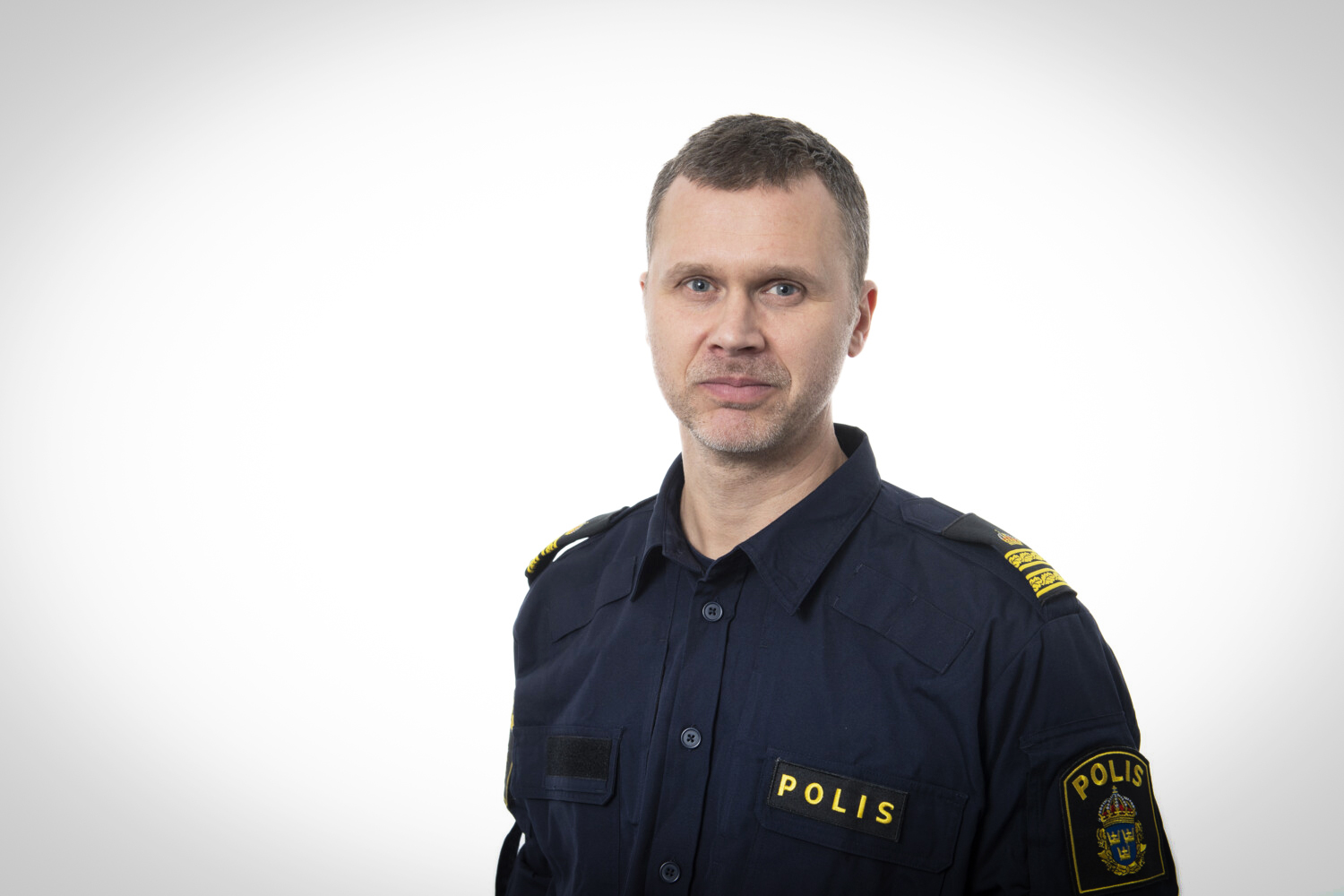 Man i polisuniform som tittar in i kameran. Vit bakgrund.