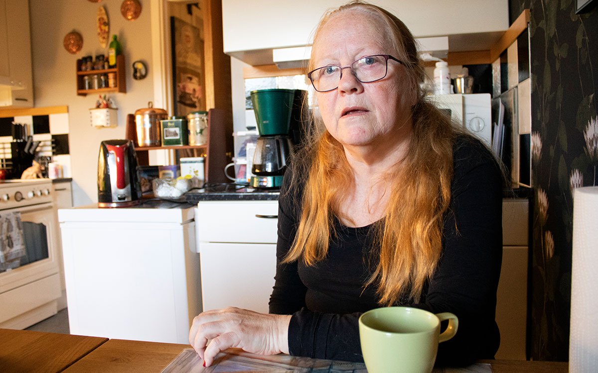 kvinna sitter vid köksbord med kaffemugg framför sig på bordet