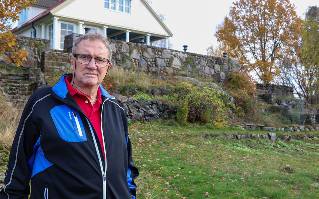 Man som står i en sluttning på tomten. I bakgrunden syns en stenmur och ett vitt hus.