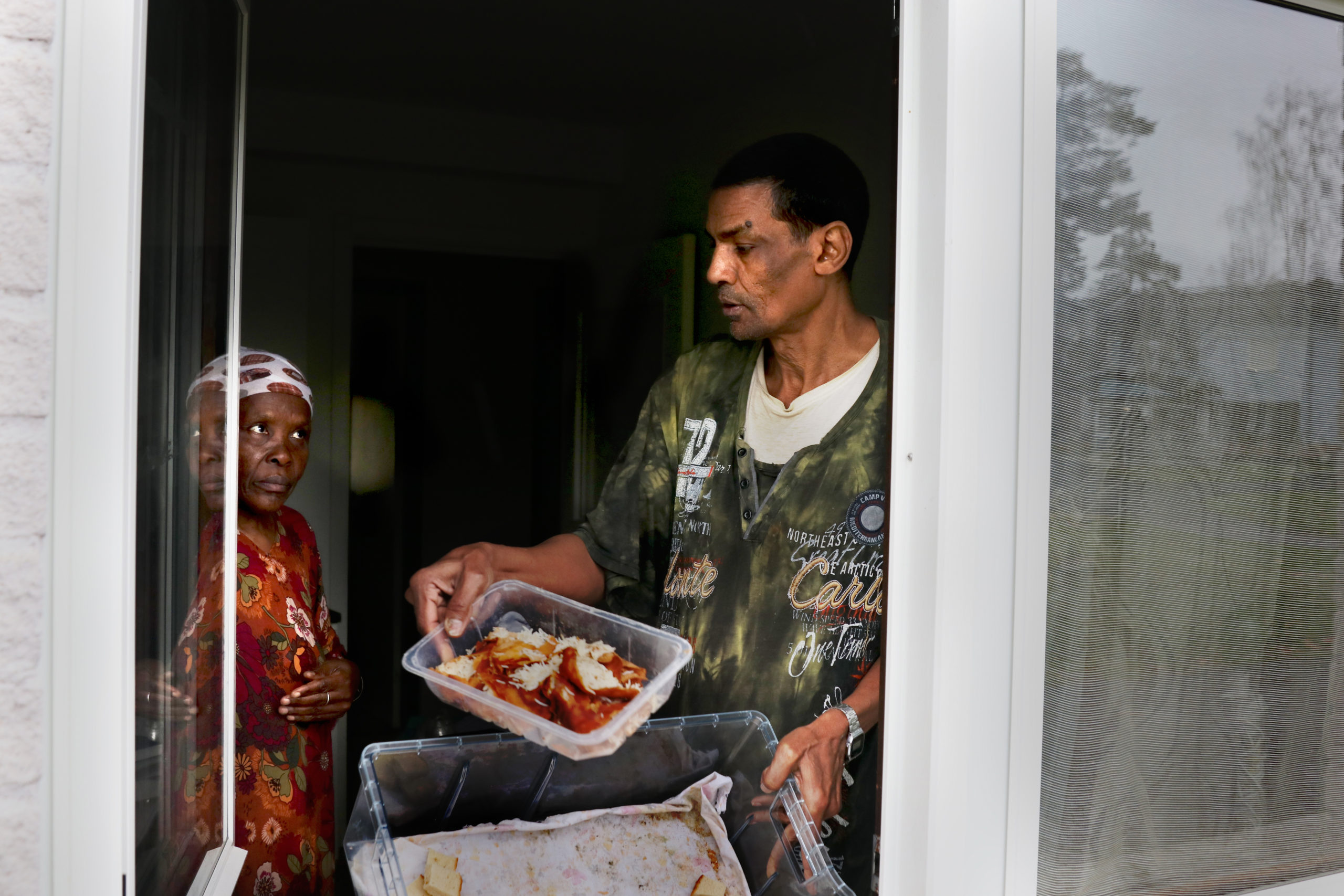 En man och en kvinna i ett fönster visar två plastbyttor med mat.