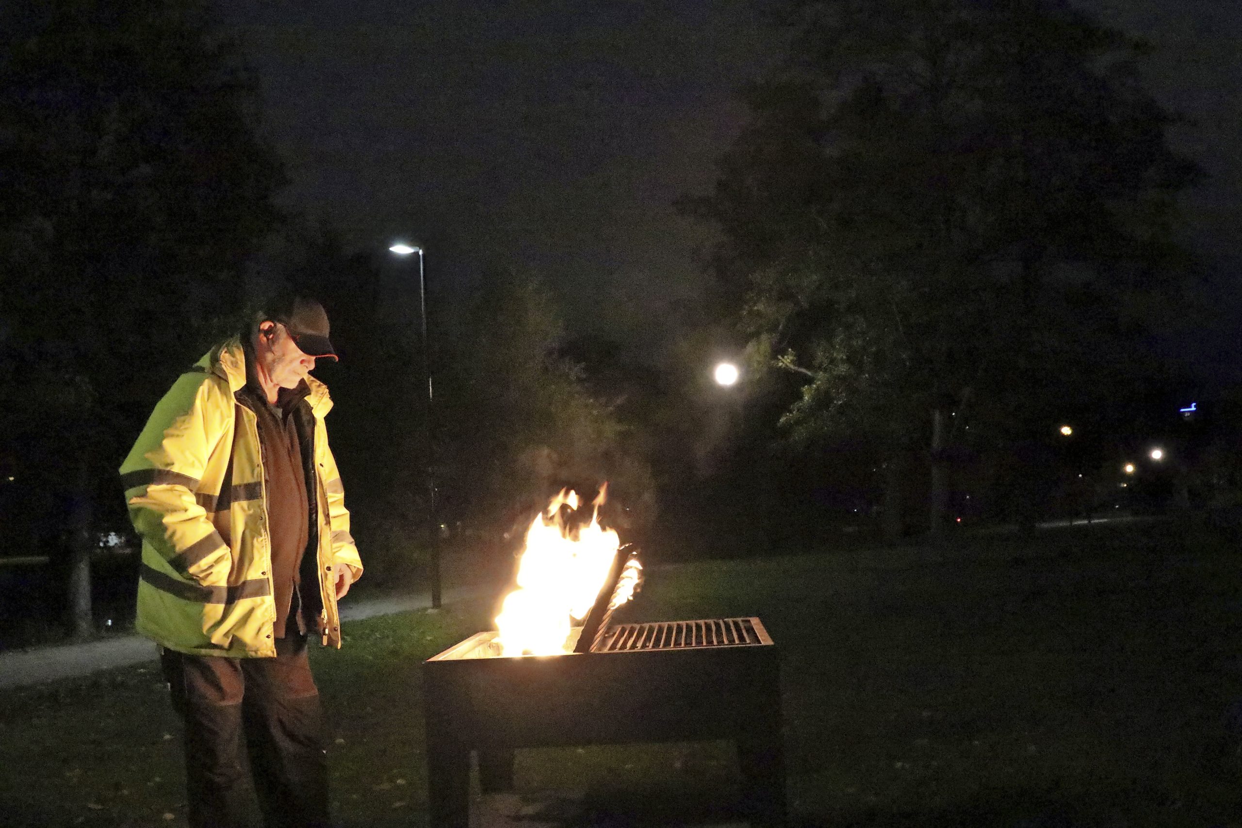 En man i gul jacka övervakar en grill med eld i.