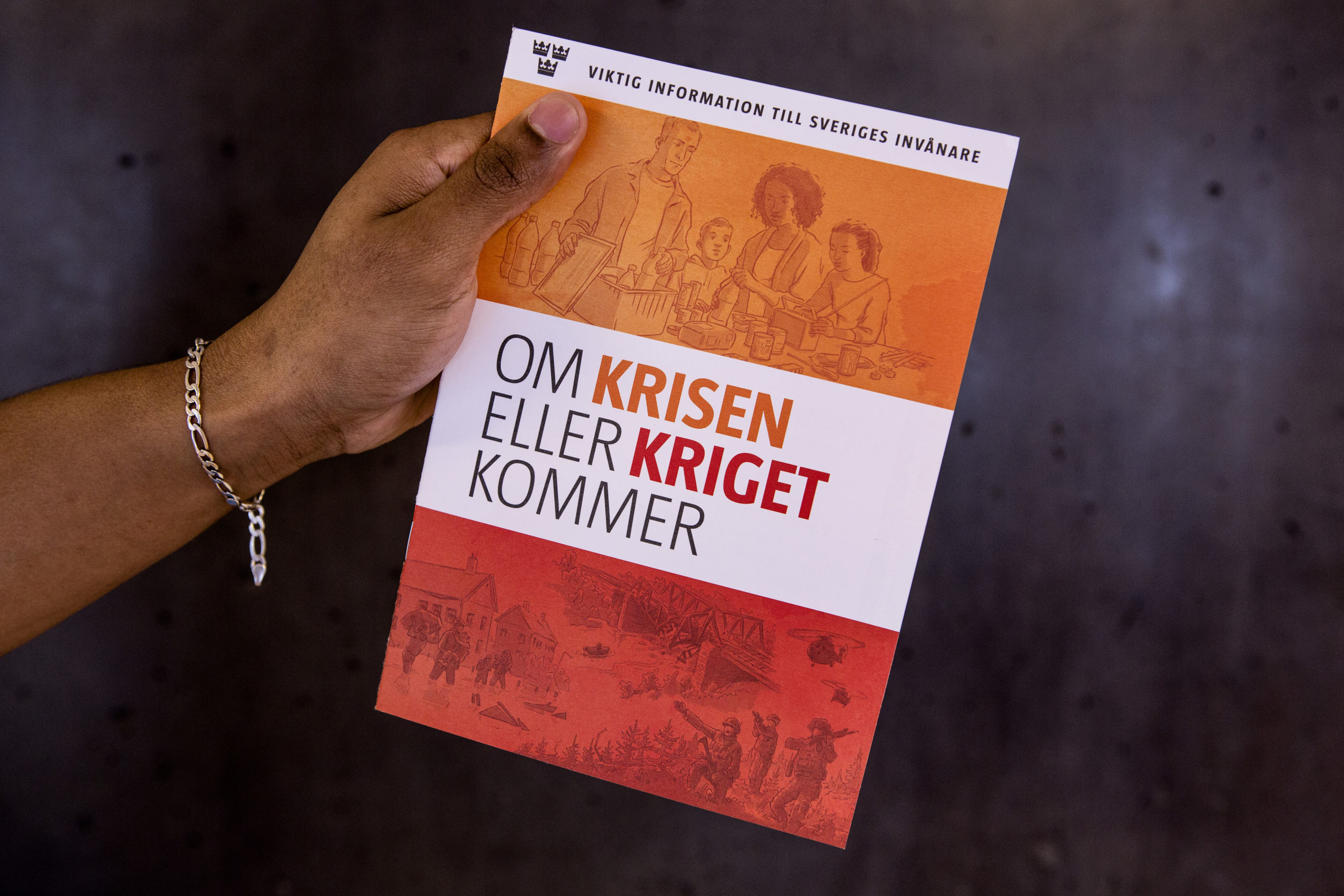 En hand håller informationsskriften "Om krisen eller kriget kommer".