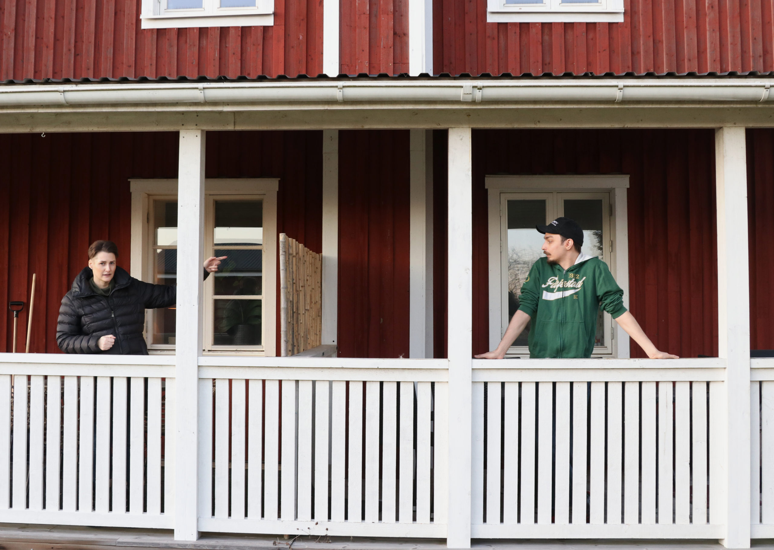 Två personer på en veranda till ett rött hus.