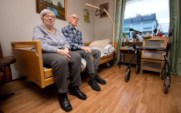Två äldre personer, en man och en kvinna, sitter på en säng i ett rum på ett äldreboende i Nässjö.