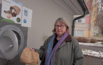 Birgitta Gustavsson med en soppåse i handen framför ett miljöhus.