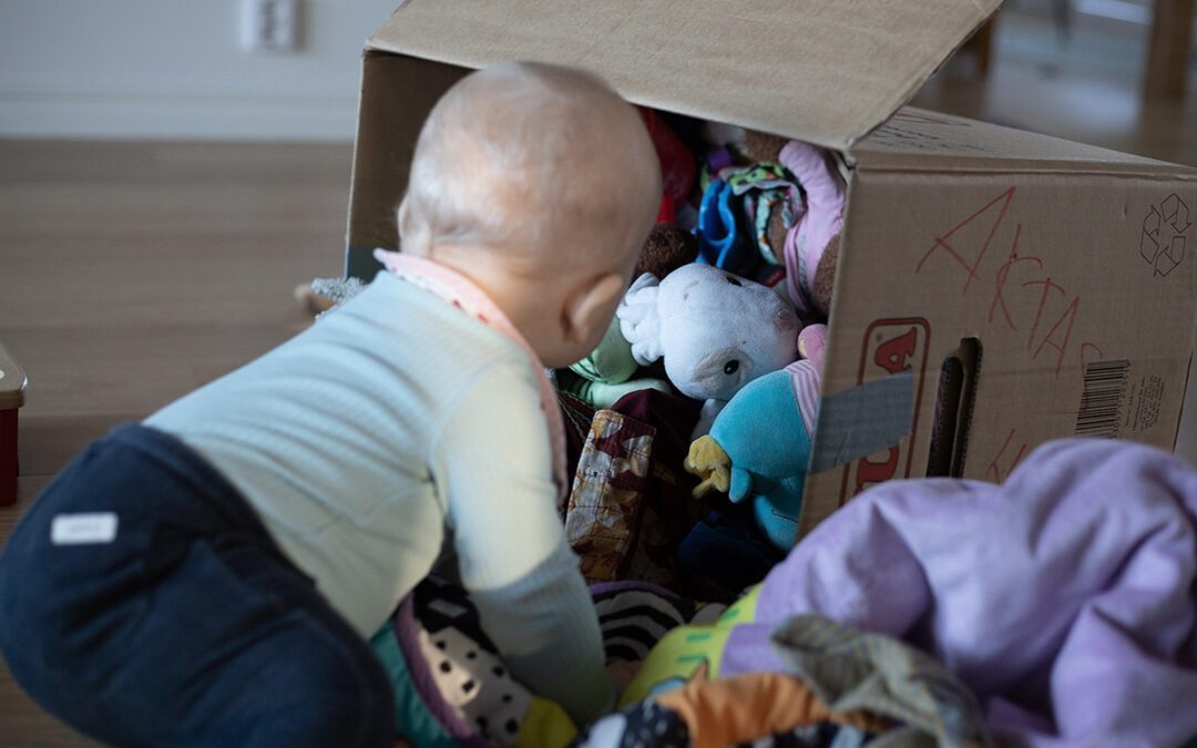 Ett litet barn packar upp sina leksaker ur en flyttlåda.