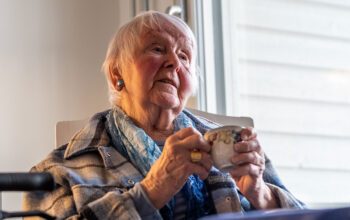 85-åriga Ingrid Ekblom i Nässjö sitter vid köksbordet med en kaffemugg i händerna.