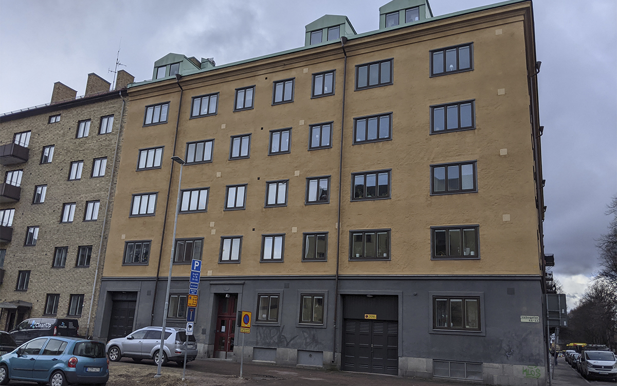 Husfasad Valbogatan 44 i Gävle, i fem våningar plus takkupor, varm sandfärgad/aprikosfärgad putsad fasad, grå fasad på nedersta våningen.