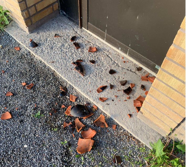 Krossade lerblomkrukor på gatan utanför en entrédörr.
