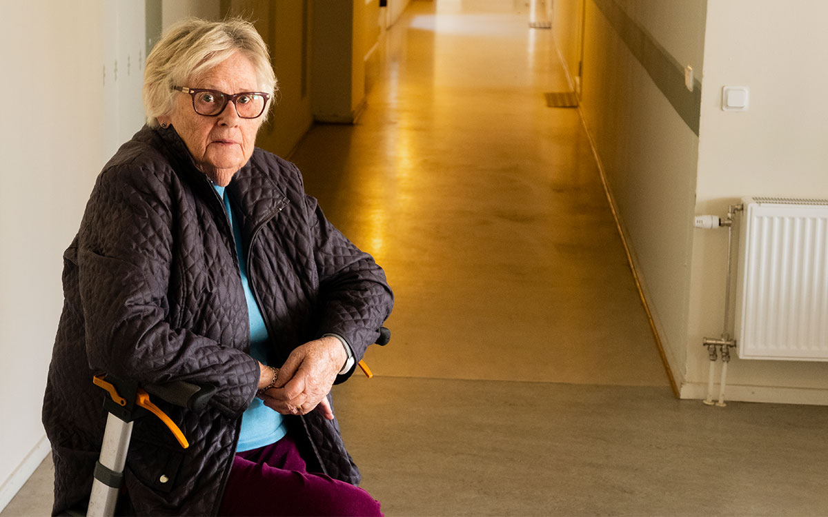 En äldre kvinna sitter på en rullator och i bakgrunden skymtar en korridor.