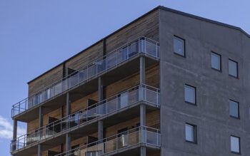 Utsnitt av tre översta våningarna på ett hus sett snett nedifrån. träfasad och balkonger åt vänster, gaveln i grått material åt höger. Blå himmel med ett litet moln i bakgrunden. Hyresgäster i tre hus i Rickomberga riskerade kraftiga hyreshöjningar på grund av en rättstvist runt om fastighetsägaren hade rätt till statligt investeringsstöd.