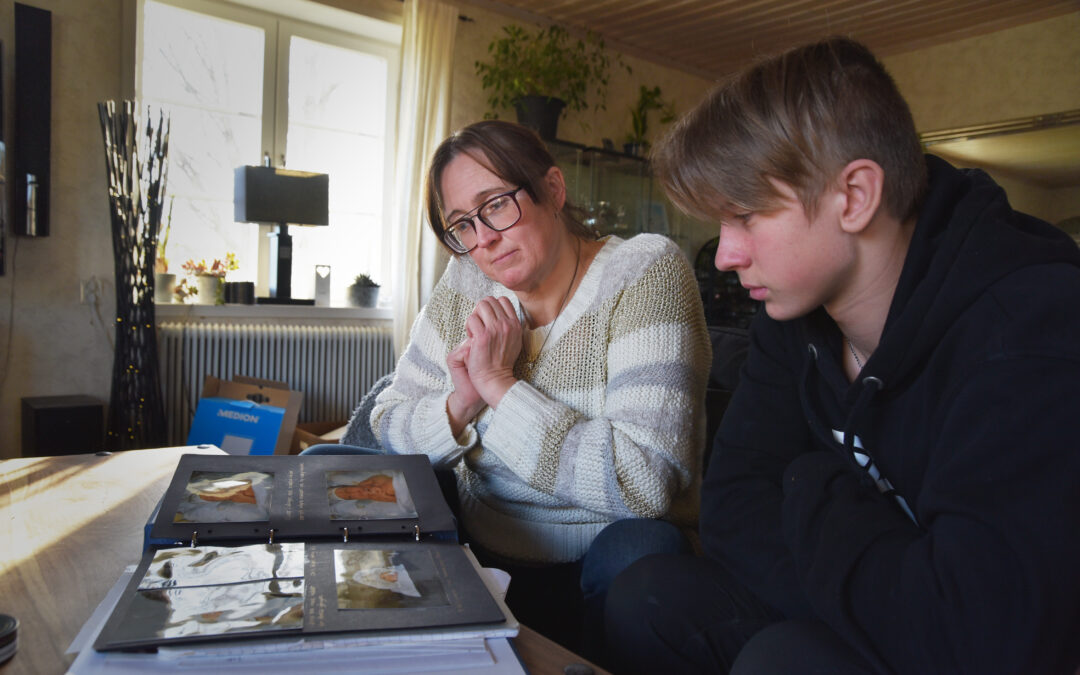 En kvinna i 40-årsåldern sitter i en soffa med sin tonårsson och bläddrar i ett fotoalbum.