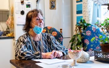 Eva Eklund sitter vid sitt köksbord. Hon behöver ofta munskydd för att kunna andas bättre, på grund av ett spåndamm i lägenheten.