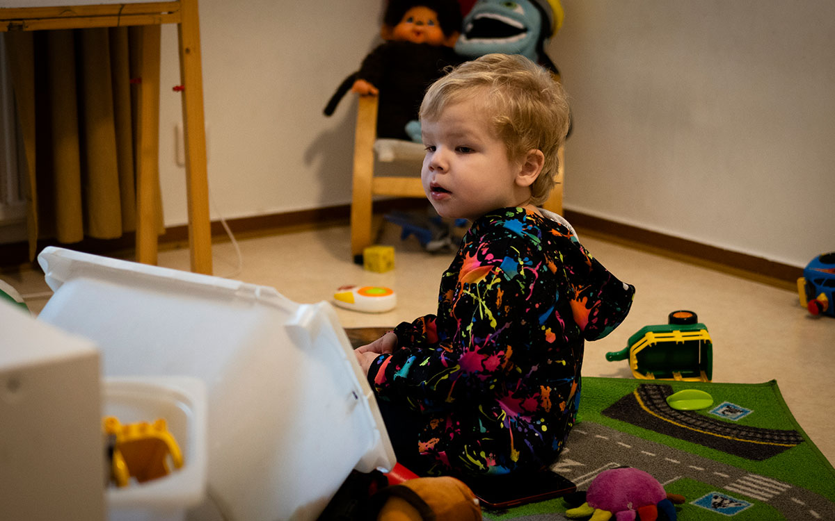En liten pojke som sitter på en lekmatta på gilvet i ett rum omgiven av leksaker.