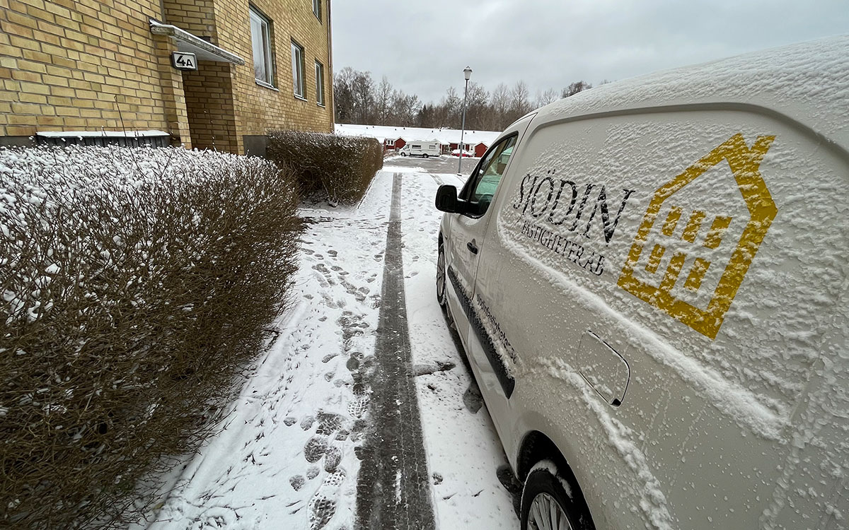 Ett flervåningshus i gult tegel och en snöig bil med texten Sjödin Fastigheter AB.