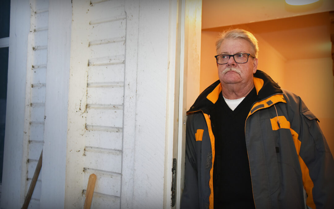 En man i 60-årsåldern lutar sig mot dörrposten in till ett hus.