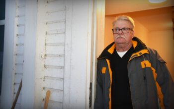En man i 60-årsåldern lutar sig mot dörrposten in till ett hus.