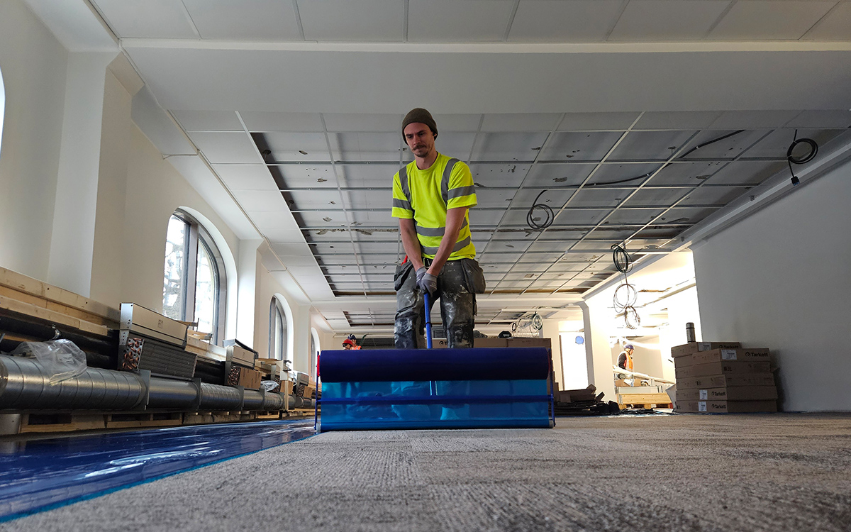 En byggarbetare lägger blå skyddsfilm över det nylagda golvet.