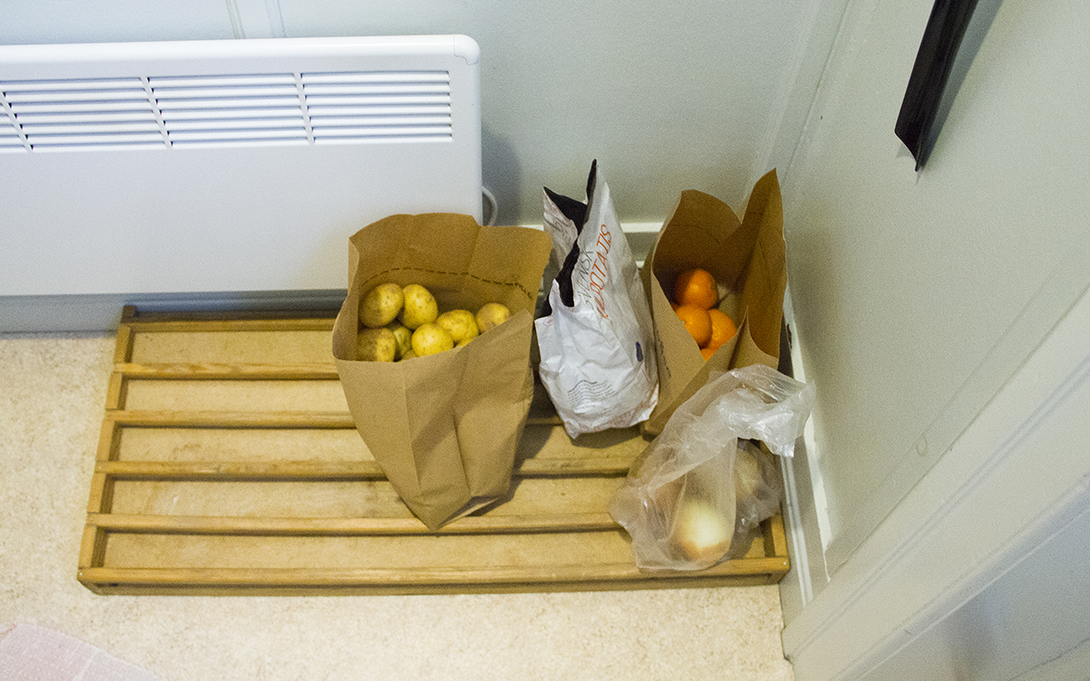 Papperspåsar och plastpåsar med bland annat potatis och apelsiner står på ett skoställ i trä.