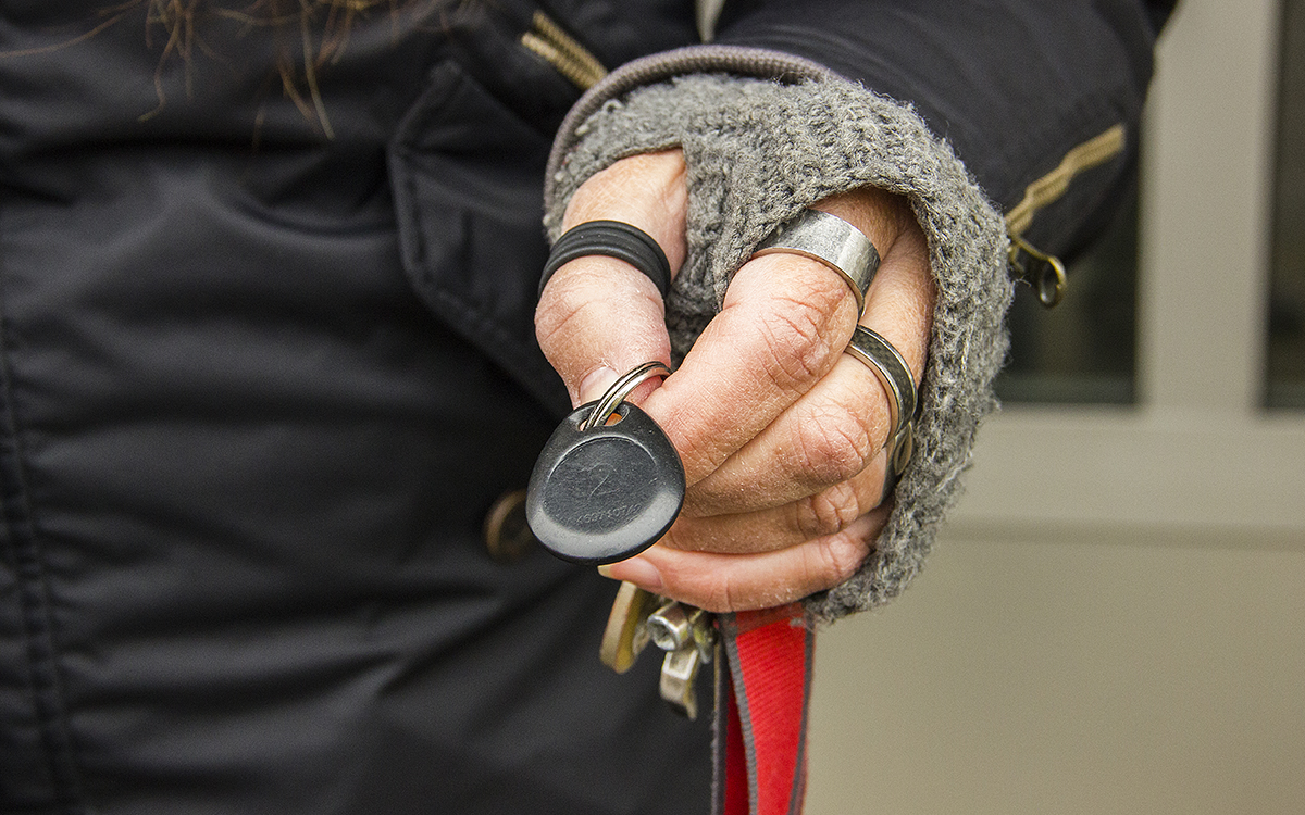 Bild på en hand med handledvärmare i grått och flera ringar, som håller i en nyckelknippa med en nyckeltagg. Hur mycket får egentligen hyresvärden snoka för att hitta bevis för svartuthyrning?