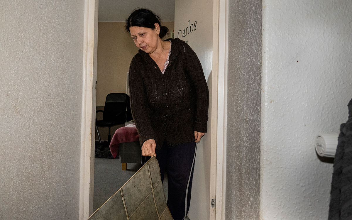 En kvinna som står i en hall i en lägenhet och lyfter på golvmattan.