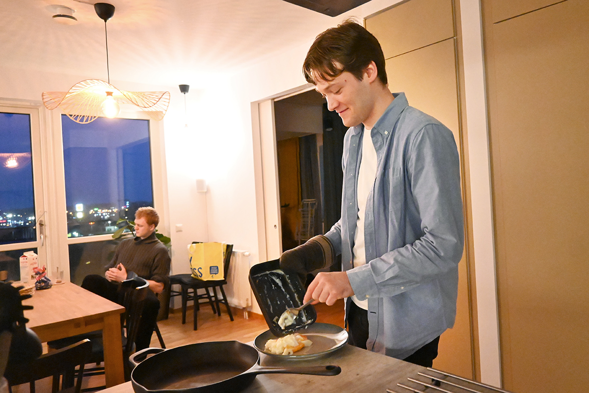 En man står vid en köksö och lägger upp mat på en tallrik.