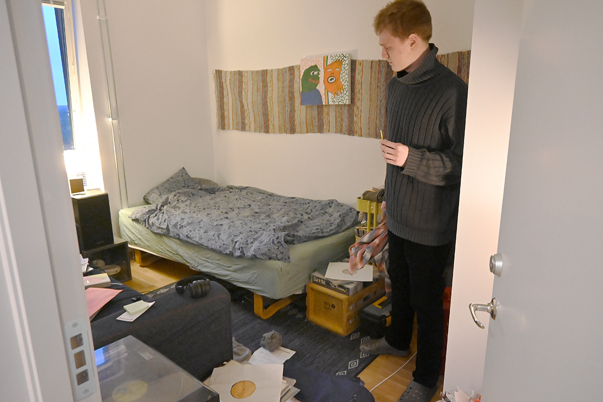 En ung man som står i ett rum med en säng och en soffa.