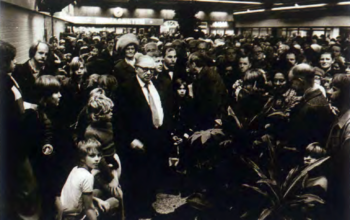 En svartvit bild där en man i kostym står i en folkmassa i ett köpcentrum.