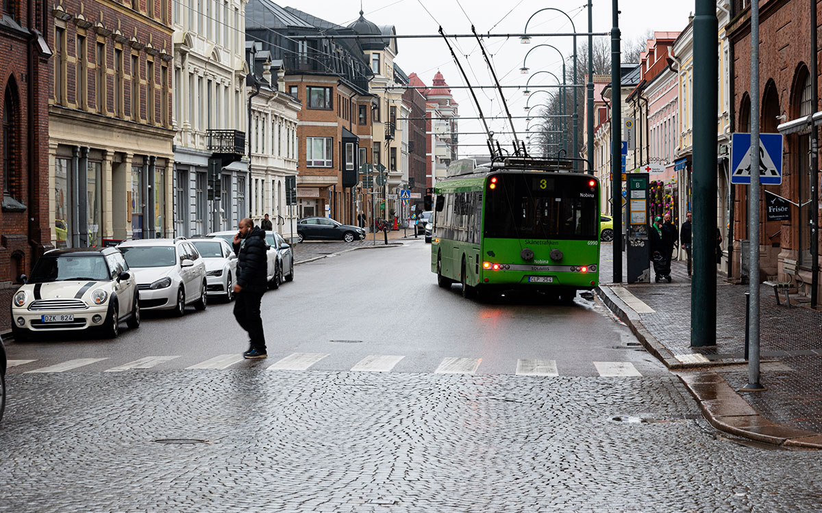 En gata men bilar, övergångsställe och en grön trådbuss.