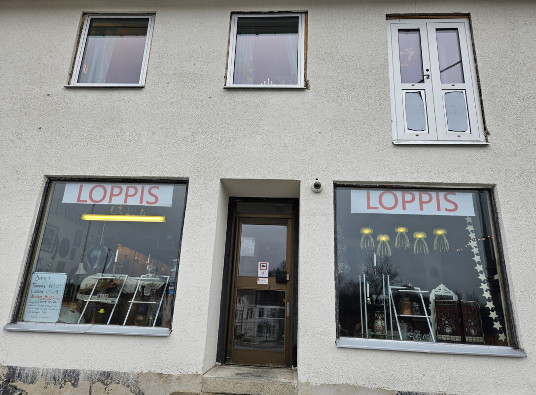 Vit fasad med fönster som visar produkter och skyltar "loppmarknad".