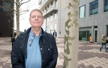 En man som står bredvid en trädstam.