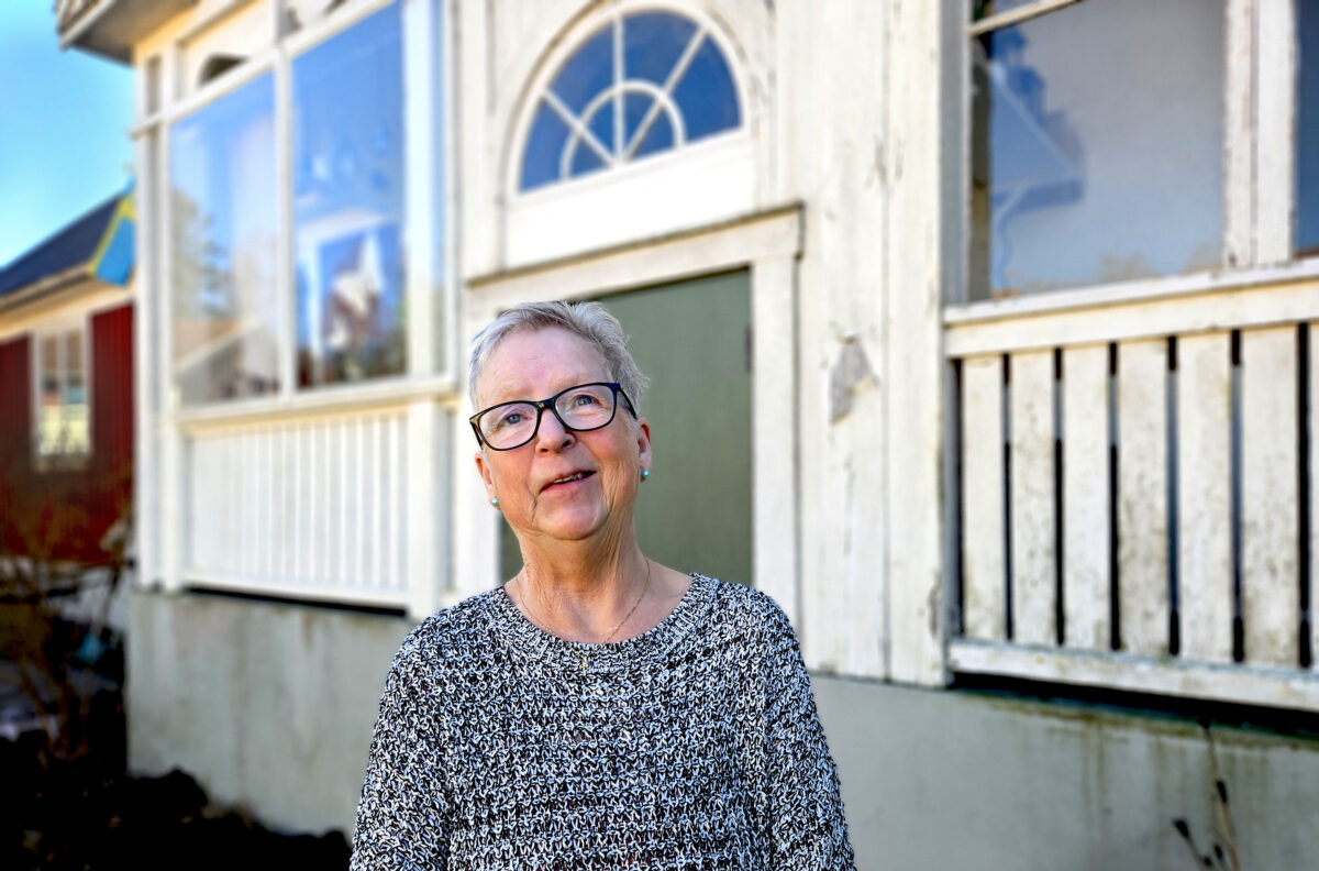 En kvinna med glasögon och en grå tröja står bredvid en balkong av glas och vanligt trä.