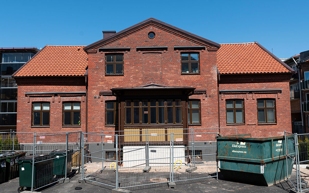 Ett äldre hus i två våningar i rött tegel med byggstaket framför.