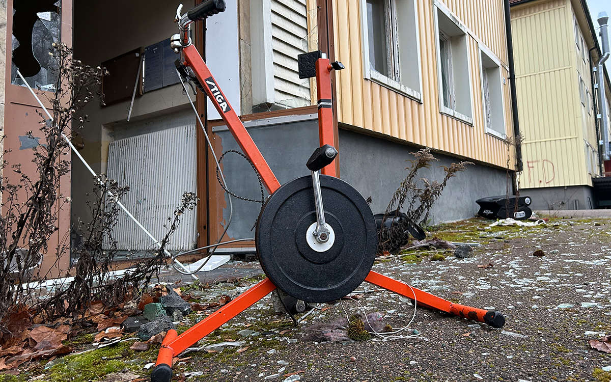En trasig, orange motionscykel utanför en port. Glaskross på marken